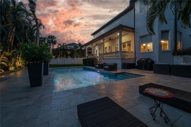 pool at dusk with ceiling fan, a patio, and grilling area