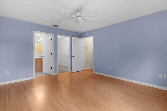 unfurnished bedroom featuring light hardwood / wood-style flooring, ensuite bathroom, a textured ceiling, a spacious closet, and a closet