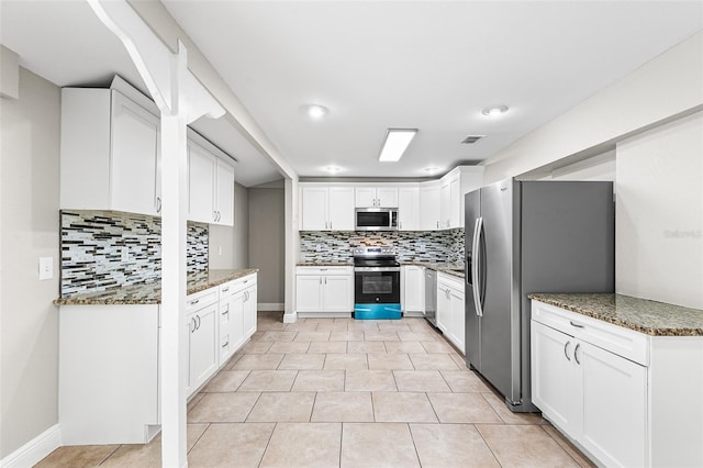 kitchen with white cabinetry, light tile patterned floors, dark stone countertops, appliances with stainless steel finishes, and backsplash