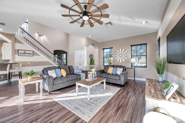 living room featuring arched walkways, ceiling fan, wood finished floors, visible vents, and stairway