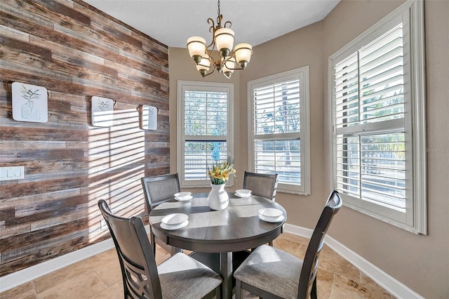 dining space with plenty of natural light, wood walls, baseboards, and an inviting chandelier