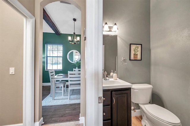 half bath with toilet, wood finished floors, beam ceiling, vanity, and a notable chandelier