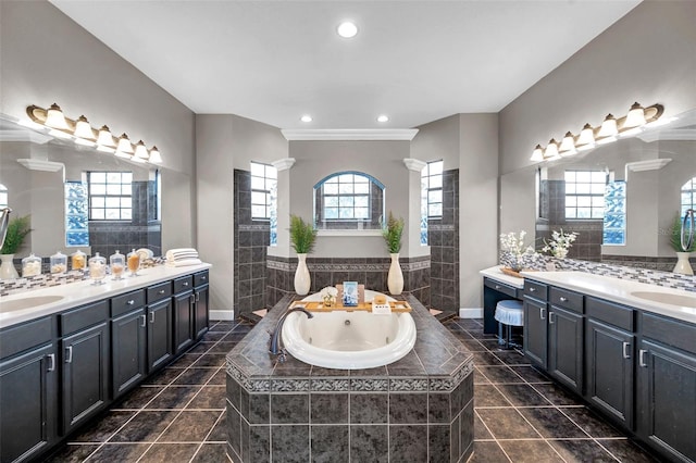 bathroom with decorative columns, two vanities, a sink, a tub with jets, and tile patterned floors