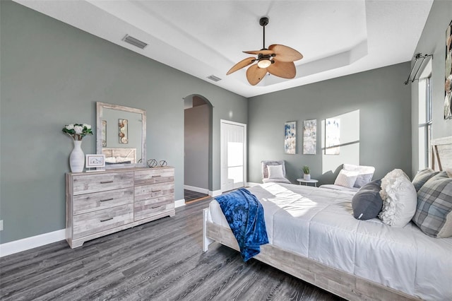 bedroom featuring dark wood-style floors, a tray ceiling, arched walkways, visible vents, and baseboards