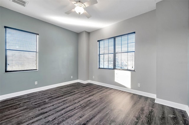 empty room with baseboards, dark wood-style flooring, visible vents, and a ceiling fan