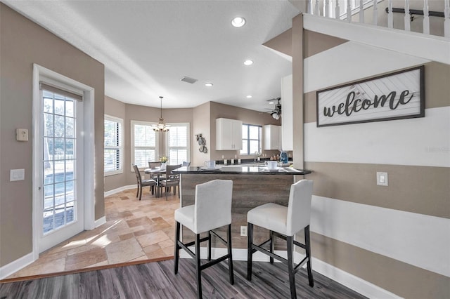 kitchen featuring decorative light fixtures, a peninsula, white cabinetry, a kitchen breakfast bar, and stone tile flooring