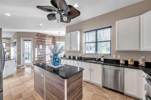 kitchen with stainless steel appliances, stone tile flooring, white cabinetry, a sink, and dark stone countertops