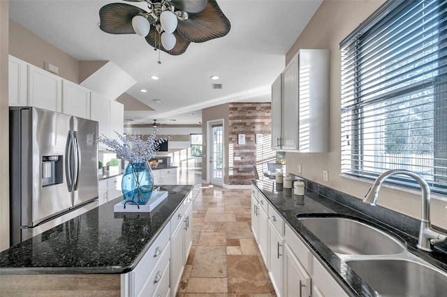 kitchen with stone tile flooring, white cabinets, a kitchen island, a sink, and stainless steel fridge