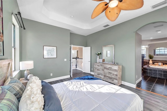 bedroom featuring baseboards, visible vents, arched walkways, wood finished floors, and a tray ceiling