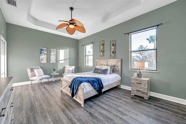 bedroom featuring dark wood finished floors, a raised ceiling, visible vents, and baseboards