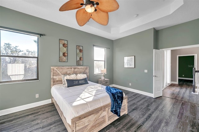 bedroom with dark wood-style floors, baseboards, a raised ceiling, and a ceiling fan