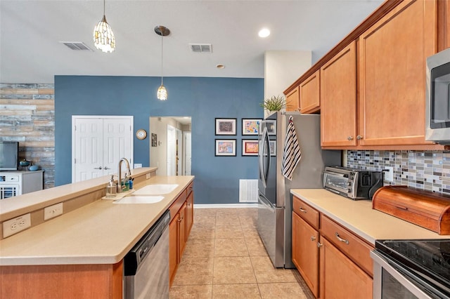 kitchen with light tile patterned flooring, appliances with stainless steel finishes, sink, hanging light fixtures, and a kitchen island with sink