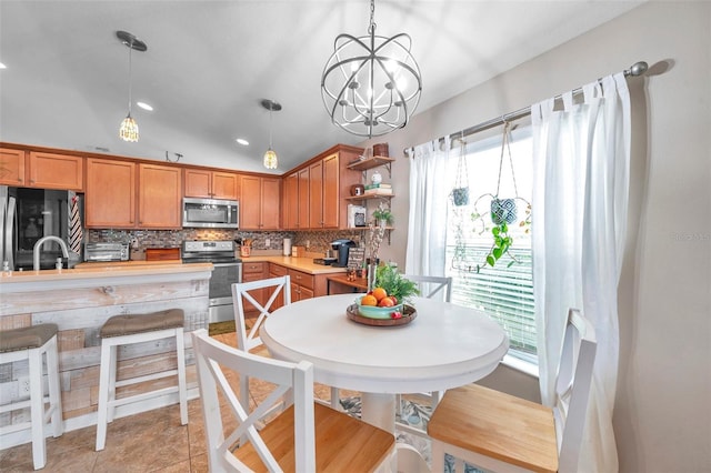 kitchen featuring lofted ceiling, hanging light fixtures, light tile patterned floors, stainless steel appliances, and decorative backsplash