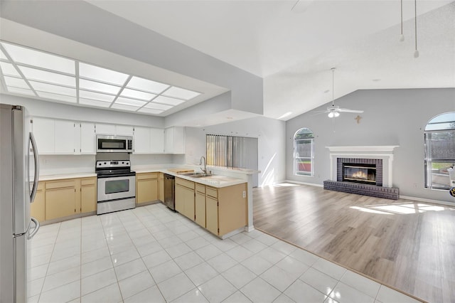 kitchen with light tile patterned flooring, sink, a brick fireplace, appliances with stainless steel finishes, and kitchen peninsula