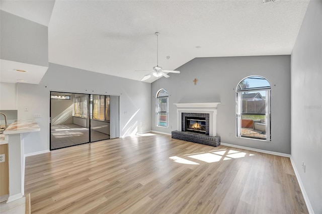 unfurnished living room featuring a brick fireplace, a wealth of natural light, lofted ceiling, and light hardwood / wood-style flooring