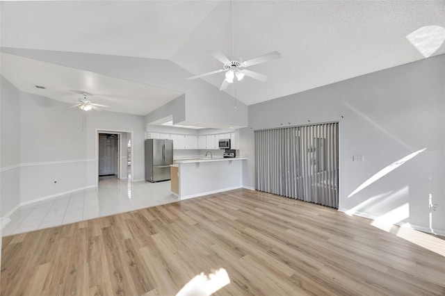 unfurnished living room with lofted ceiling, sink, ceiling fan, light hardwood / wood-style floors, and a textured ceiling