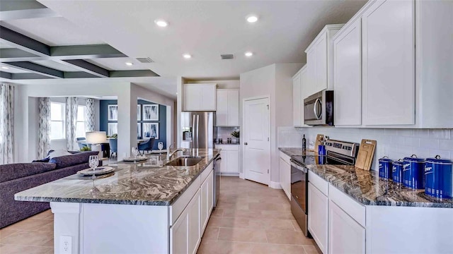 kitchen featuring a spacious island, white cabinets, stainless steel appliances, beamed ceiling, and sink