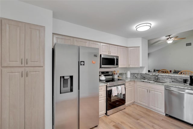 kitchen featuring sink, light hardwood / wood-style flooring, appliances with stainless steel finishes, ceiling fan, and light stone countertops