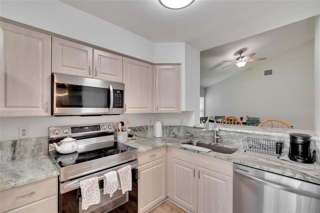 kitchen featuring lofted ceiling, sink, light stone counters, ceiling fan, and stainless steel appliances