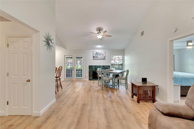 dining area featuring a tiled fireplace, ceiling fan, high vaulted ceiling, and light wood-type flooring