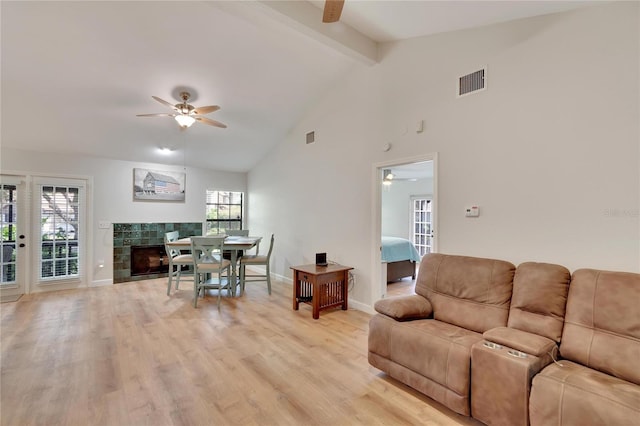 living room with beamed ceiling, a tile fireplace, a healthy amount of sunlight, and light wood-type flooring