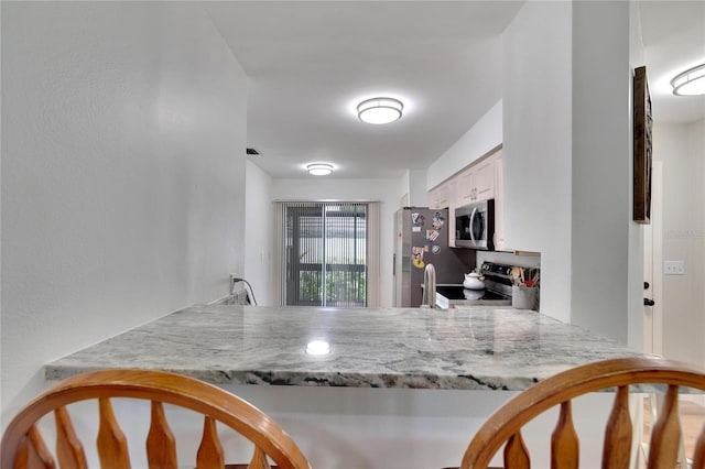 kitchen with stainless steel appliances, white cabinets, and light stone counters