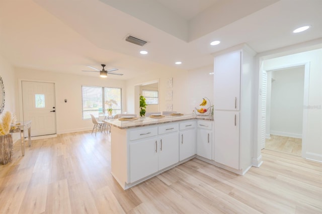 kitchen featuring kitchen peninsula, light wood-type flooring, white cabinetry, and light stone countertops