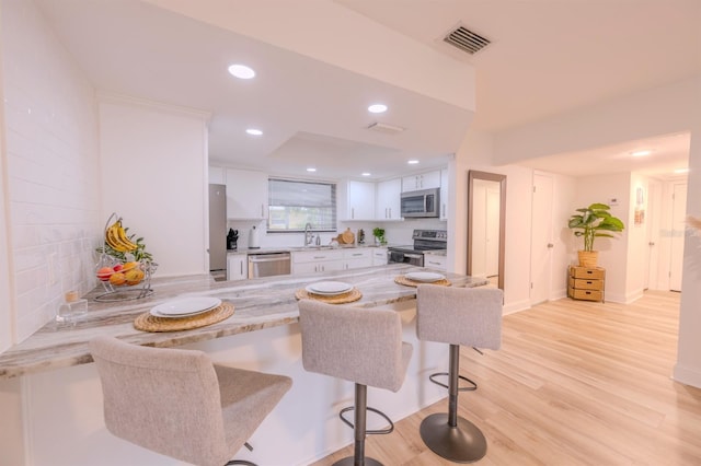 kitchen with appliances with stainless steel finishes, white cabinets, sink, light hardwood / wood-style flooring, and a breakfast bar area