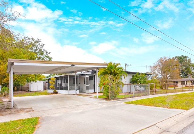 view of front of house featuring a carport, a sunroom, a front lawn, and a storage shed