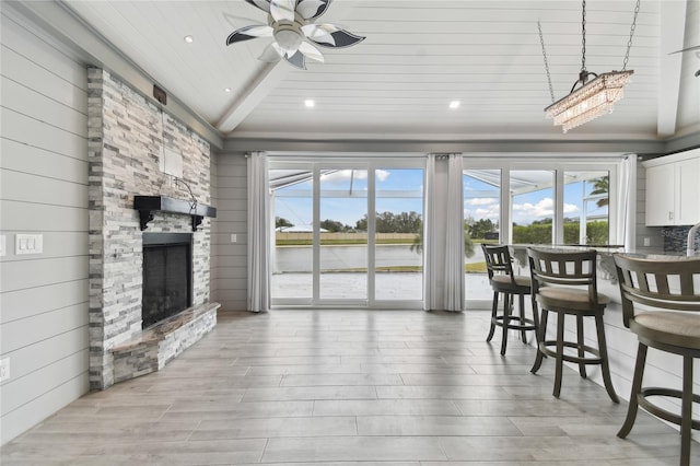 interior space featuring lofted ceiling, a stone fireplace, a water view, ceiling fan, and wooden ceiling