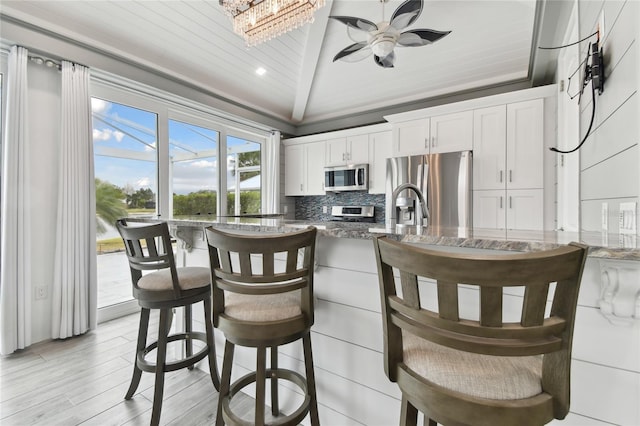 kitchen featuring appliances with stainless steel finishes, wood ceiling, white cabinetry, dark stone counters, and backsplash