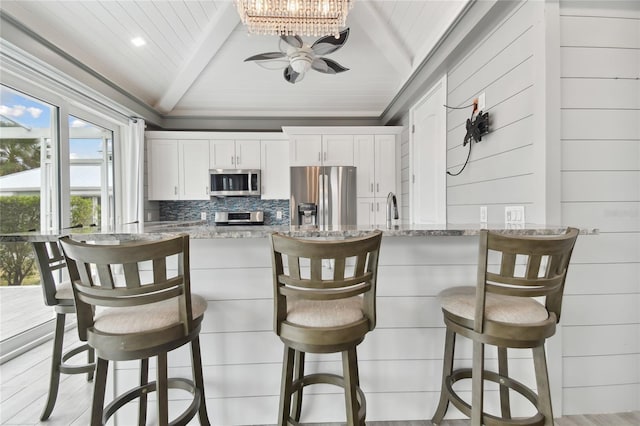 kitchen featuring white cabinets, decorative backsplash, light stone countertops, a breakfast bar area, and stainless steel appliances