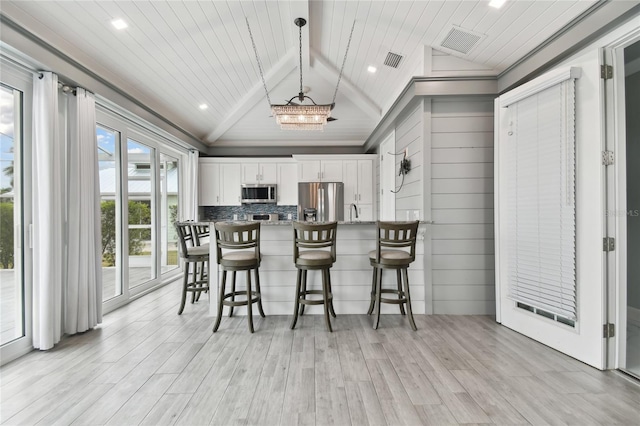 kitchen with white cabinets, decorative light fixtures, stainless steel appliances, lofted ceiling with beams, and light wood-type flooring