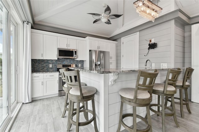 kitchen featuring white cabinetry, vaulted ceiling with beams, stone counters, a breakfast bar area, and stainless steel appliances