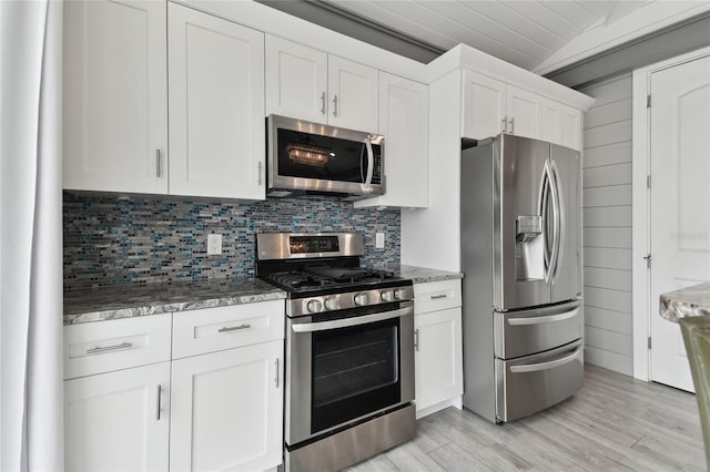 kitchen featuring white cabinets, lofted ceiling, stainless steel appliances, tasteful backsplash, and light wood-type flooring