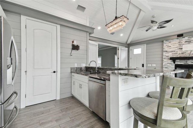 kitchen featuring pendant lighting, white cabinets, appliances with stainless steel finishes, a kitchen bar, and lofted ceiling with beams