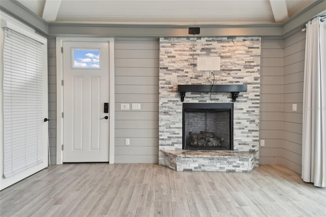 unfurnished living room featuring light hardwood / wood-style flooring, a stone fireplace, and wooden walls