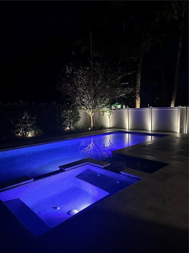 pool at twilight featuring an in ground hot tub