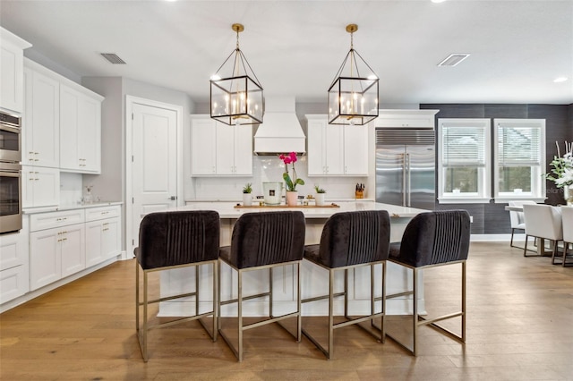 kitchen with built in refrigerator, premium range hood, a center island, and decorative light fixtures