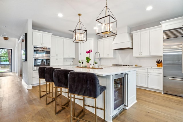 kitchen featuring appliances with stainless steel finishes, pendant lighting, wine cooler, custom exhaust hood, and a center island with sink