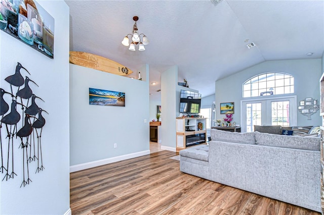 living room featuring hardwood / wood-style floors, a notable chandelier, vaulted ceiling, and french doors