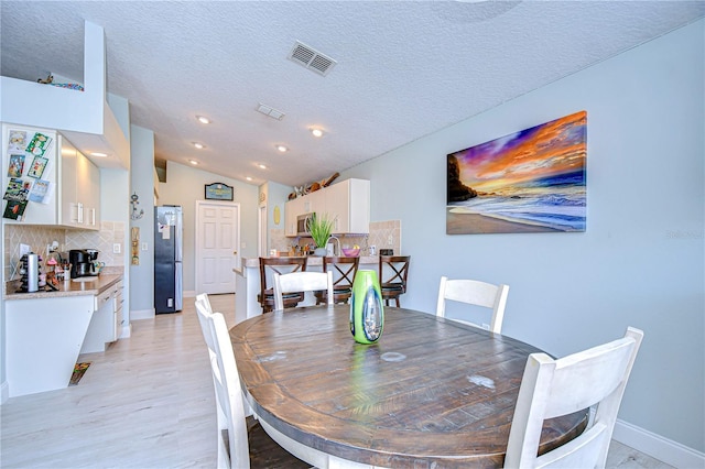 dining room with light hardwood / wood-style flooring, vaulted ceiling, and a textured ceiling