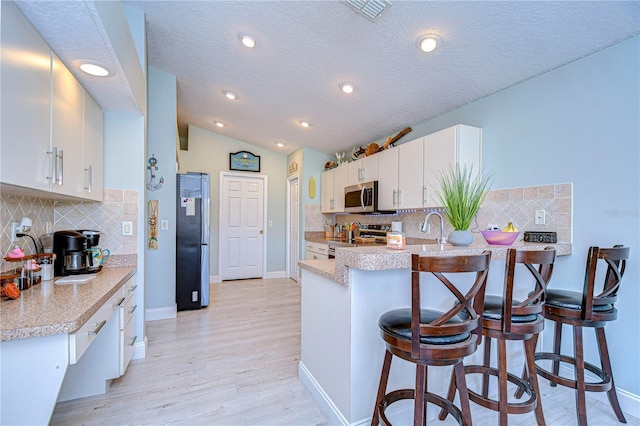 kitchen with lofted ceiling, a breakfast bar, white cabinetry, appliances with stainless steel finishes, and kitchen peninsula