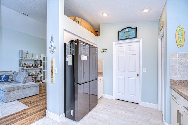 kitchen with a textured ceiling, white cabinets, stainless steel refrigerator, and light hardwood / wood-style floors