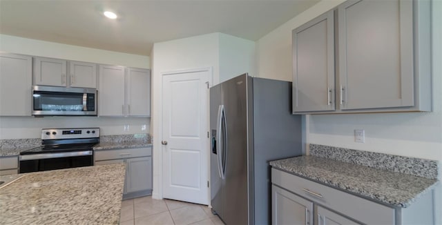 kitchen with light stone counters, appliances with stainless steel finishes, gray cabinets, and light tile patterned floors