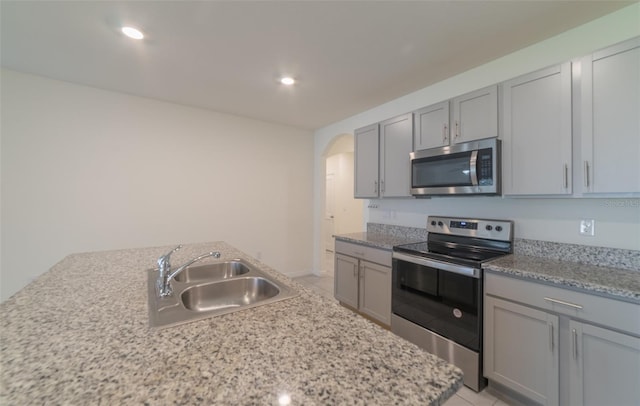 kitchen with stainless steel appliances, light stone countertops, sink, and light tile patterned floors