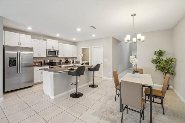 kitchen featuring a kitchen bar, stainless steel appliances, dark stone counters, and an island with sink