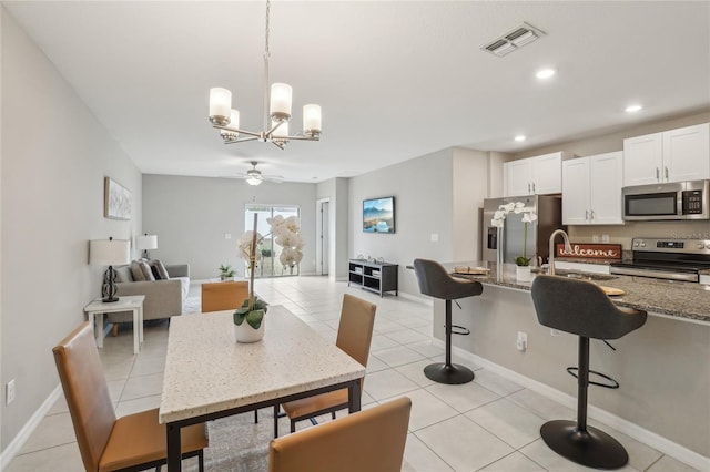 dining space featuring sink, light tile patterned flooring, and ceiling fan with notable chandelier