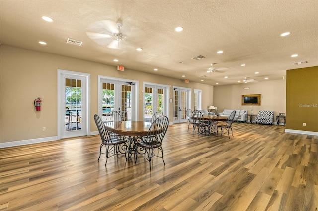 dining room featuring light wood-type flooring, a textured ceiling, ceiling fan, and french doors