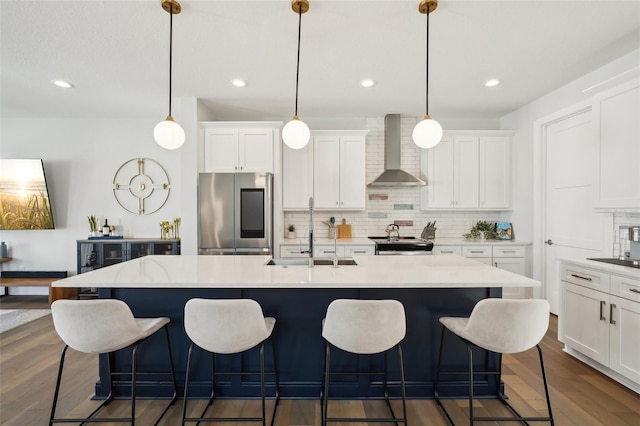 kitchen with pendant lighting, wall chimney range hood, sink, a kitchen island with sink, and stainless steel appliances